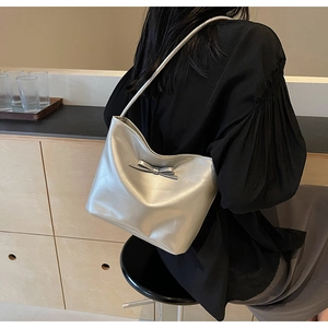 Sac bandoulière argenté brillant avec nœud porté par un mannequin dans un décor épuré