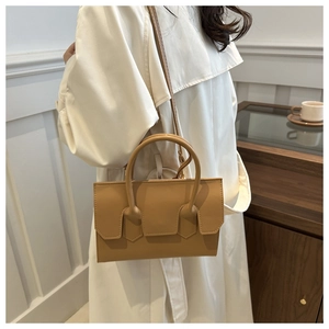 Detail of light khaki crossbody bag with rounded handle shown in a chic lifestyle setting