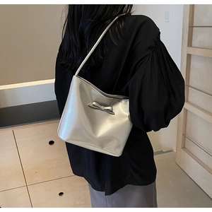 Shoulder shot of a silver glossy bucket bag with a bow accent on a female model