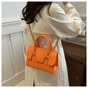 Chic orange faux leather mini tote bag with crossbody strap shown on a white trench coat