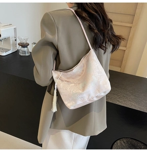Detail of light pink floral brocade hobo bag with white tassel on shoulder of a model