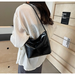 Minimalist black patent leather hobo bag with bow detail on a shoulder-wearing model