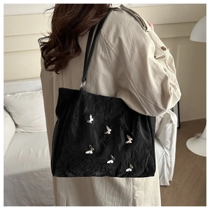 Detail view of black tote bag featuring silver butterfly metal charms and crinkled texture