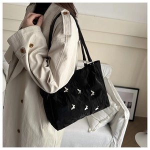 Detail of black tote bag with butterfly charms and pleated texture on woman's shoulder