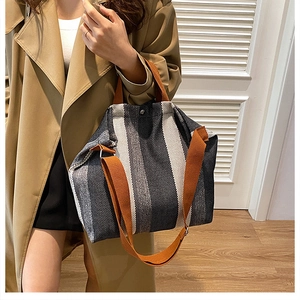 Detail of striped tote bag with orange handles and adjustable shoulder strap attachment