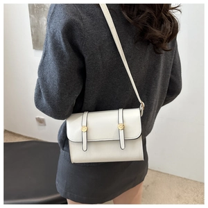Detail of white leather crossbody bag featuring twin straps and gold circular hardware