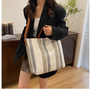Vertical striped canvas tote bag with brown leather straps shown on shoulder by model