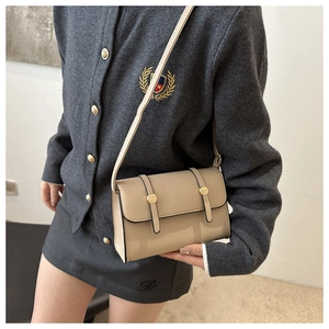Detail view of a beige crossbody bag with gold hardware worn on a grey knit sweater