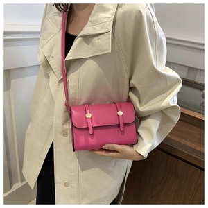 Close-up of bright pink leather messenger bag with gold metal buckles on a trench coat