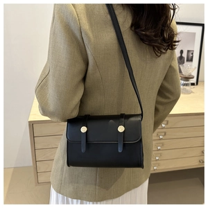 Detail view of a black flap crossbody bag with golden buckle and leather strap on model