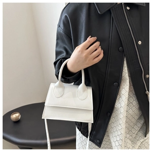White glossy patent leather trapezoid handbag worn with a black jacket and lace skirt
