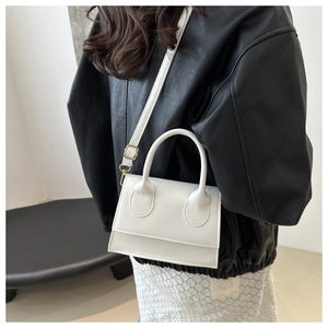 White mini crossbody bag with a curved handle shown on a model wearing a black leather jacket