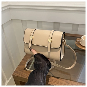 Detail of a beige crossbody messenger bag with gold metal buckles and black edge finish