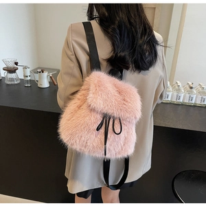 Pink faux fur backpack with black drawstring closure shown on model in a cafe