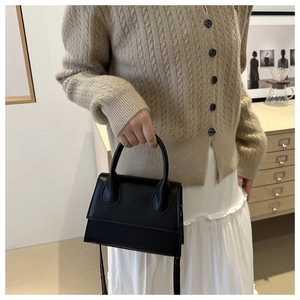 Detail of a black leather crossbody bag with a curved handle shown in a minimal interior