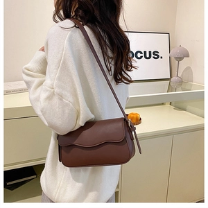 Detail of a dark brown crossbody bag with a wavy flap and adjustable leather strap