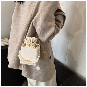 Detail of white lace embossed bucket bag with pearl handle and golden chain strap