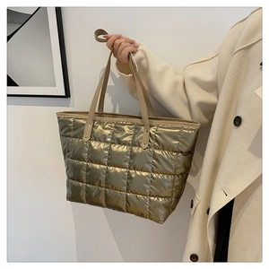 Detail of metallic gold quilted tote bag featuring large grid texture and brown handles