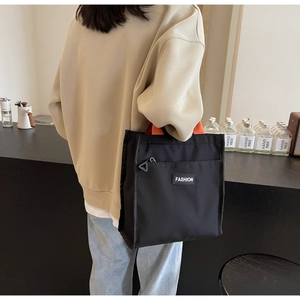 Minimalist black lunch bag with orange handles and front zipper pocket close-up detail