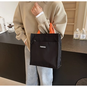 Detail of nylon handbag with black body, orange handles and front zipper pocket