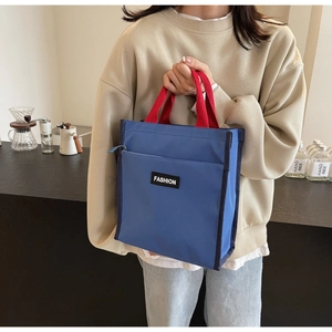 Detail of blue nylon lunch tote with red handles and FASHION label in a cafe setting