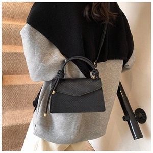 Detail view of black woven texture handbag with knot handle and golden hardware details