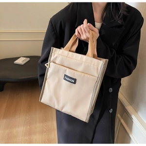 Detail of minimalist beige nylon lunch tote with fashion label and brown woven handles