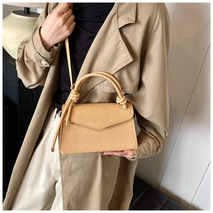 Detail of beige quilted woven handbag with knot handle and detachable shoulder strap