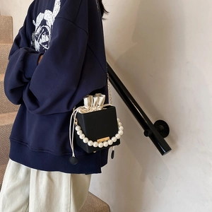 Minimalist black square bucket bag featuring large pearl handle and chain strap