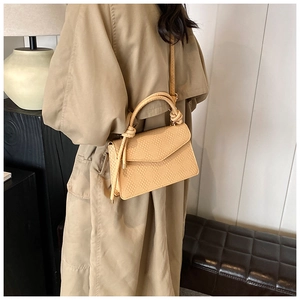 Detail of beige woven texture handbag with dual knot handle and adjustable shoulder strap
