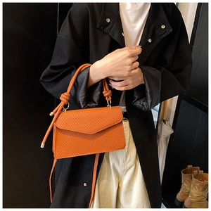 Detail shot of bright orange woven handbag with cord knot handle and textured pattern