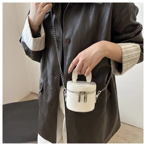 Detail of mini white cylinder bucket bag with silver chain and dual zipper on leather jacket