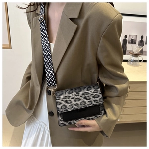 Detail of grey leopard print flap and wide geometric shoulder strap on black crossbody bag