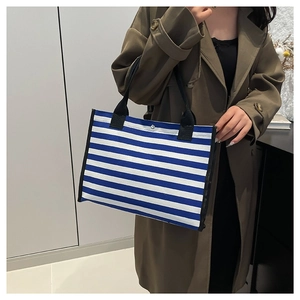 Borsa tote in tela a righe blu e bianche con manici neri indossata da una modella