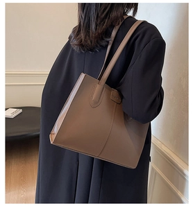 Detailed view of a brown vintage tote bag worn over a black coat showing size and texture