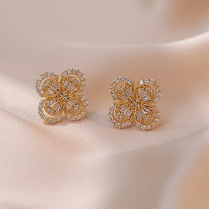 Golden clover stud earrings with sparkling zircon crystals on champagne silk background