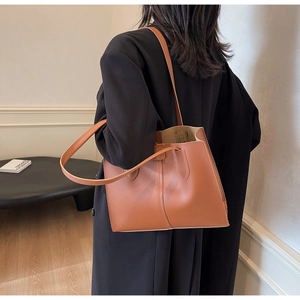 Caramel leather tote bag featuring a decorative seam and long shoulder strap on a model