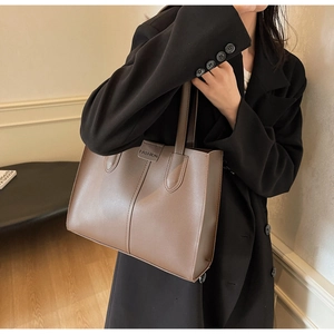 Close-up of a large brown tote bag with leather straps on a model in a black blazer