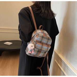Detail of plaid patterned backpack with brown leather straps and pink plush pendant