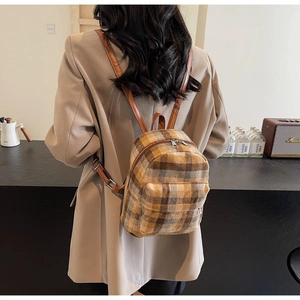 Close-up of brown plaid backpack with leather straps and metal zippers on a model