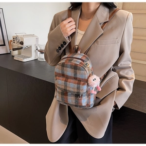 Plaid wool backpack with brown leather straps and pink plush charm shown in a lifestyle setting