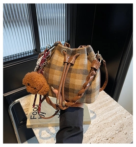 Détail du sac seau en laine à carreaux marron avec anse tressée et breloque peluche