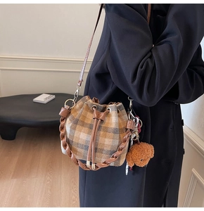 Detail of checkered bucket bag featuring woven handle and a cute plush bear charm