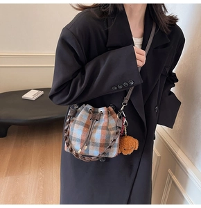 Detailed view of plaid bucket bag with leather drawstring and plush bear charm