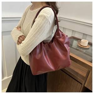 Detail view of burgundy pleated leather underarm bag on a model in minimalist interior