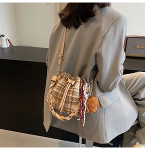 Detail of plaid bucket bag with woven handle and cute bear charm in cozy autumn setting