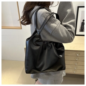 Minimalist black soft leather tote bag with pleated detail shown on person in cozy interior
