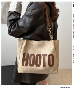 Detail of suede tote bag with brown letter patch and gold metal chain strap