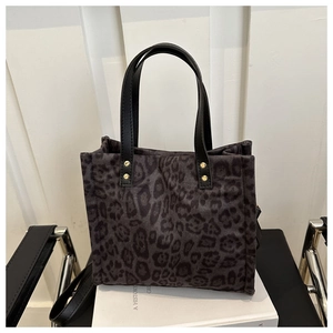 Detail of leopard print tote bag with black leather handles and gold rivet accents