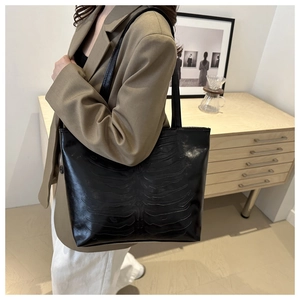 Detail of black tote bag with unique bone-shaped embossing and glossy crocodile texture